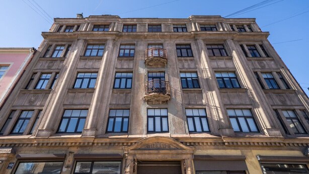 Un immeuble à étages doté d’une façade symétrique, de grandes fenêtres et d’un balcon central orné de balustrades décoratives.