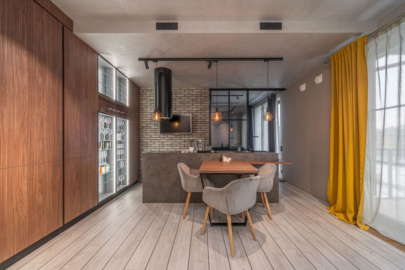 Une cuisine moderne avec un mur en briques, des armoires en bois et un coin repas comprenant une table et des chaises en bois.