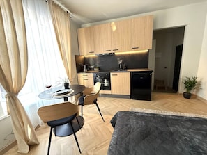 Cozy apartment with a kitchenette, dining area, and comfortable bed, set against a herringbone-patterned floor.