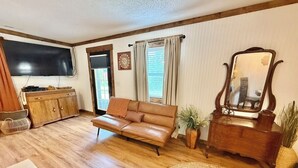 A living room with a brown leather sofa, a wooden cabinet, a mirror, and a television on the wall.