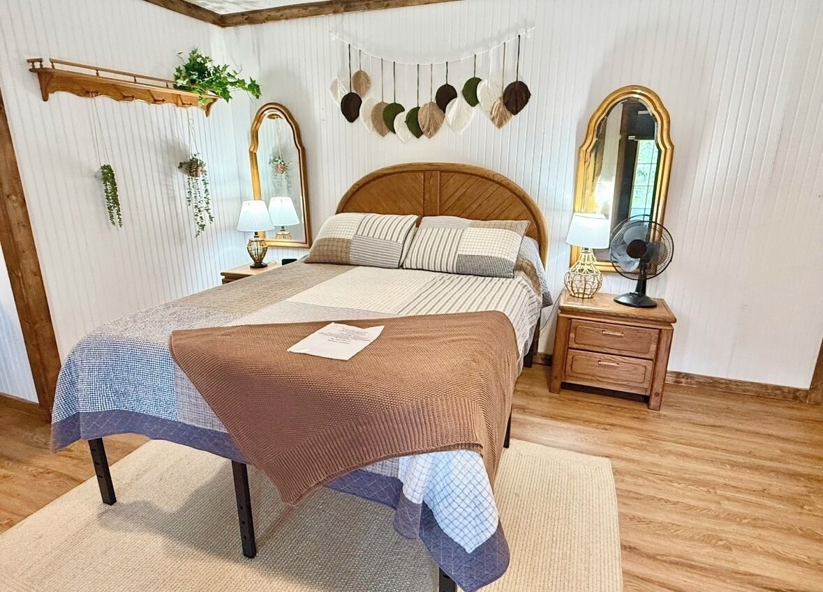 A bedroom with a wooden bed, two bedside tables with lamps, a mirror, and decorative wall hangings.