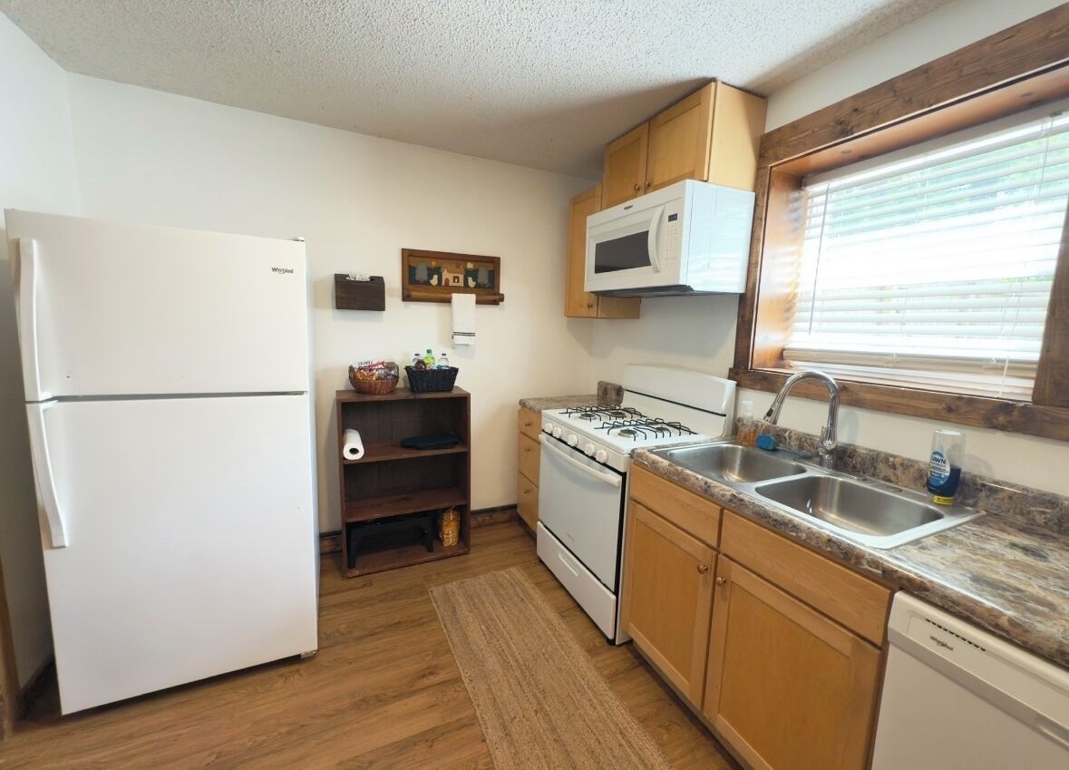 A compact kitchen with a refrigerator, stove, microwave, sink, and wooden cabinets.
