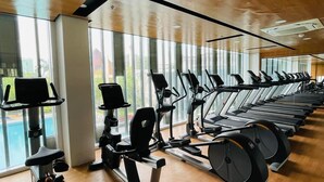 A gym with rows of treadmills and elliptical machines, large windows, and wooden flooring.