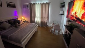A bedroom with a bed, bedside table, lamp, TV, and a small table with chairs.