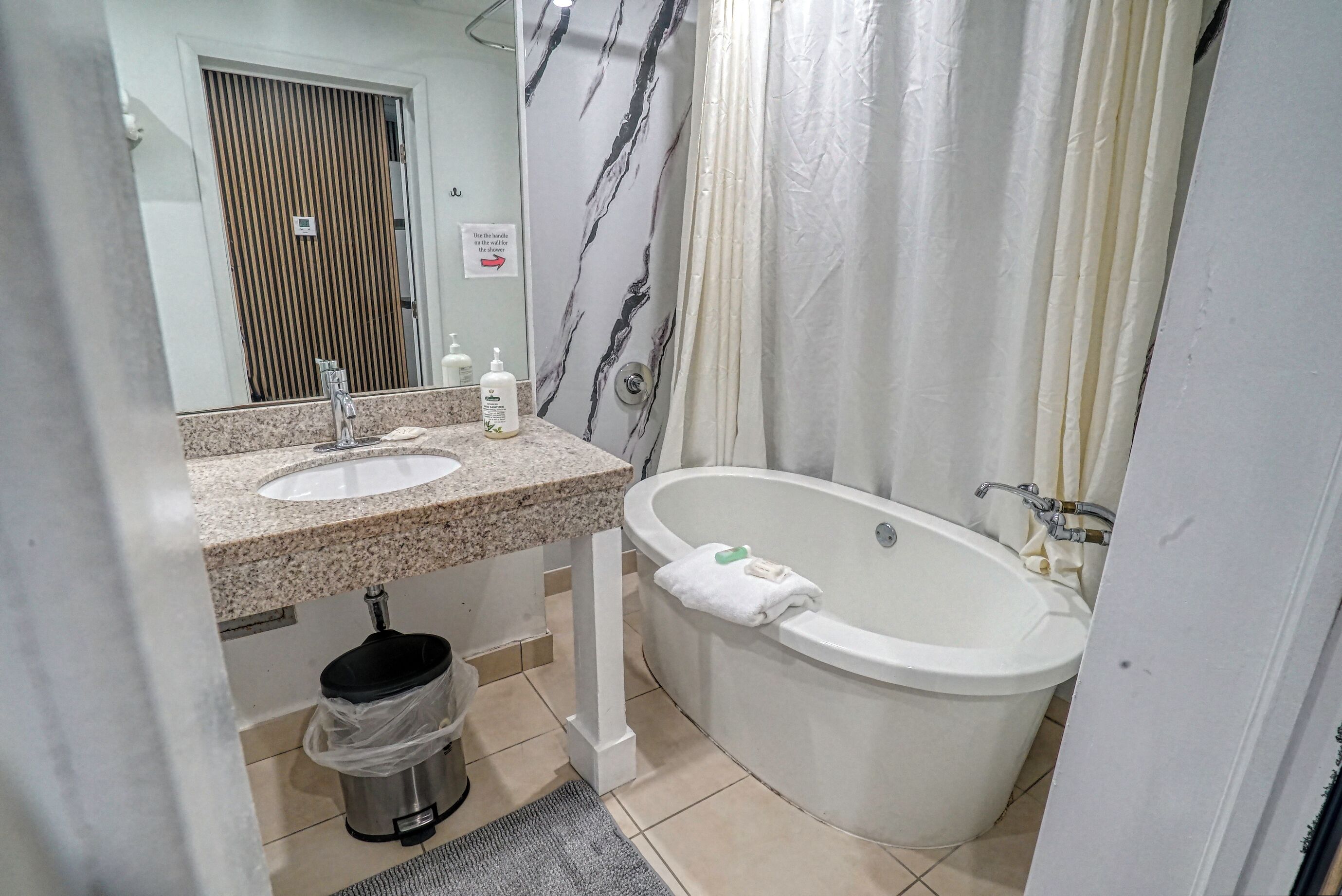 Casa de banho com duas pias, uma banheira, cortina de chuveiro, sanita e um cestinho de lixo.