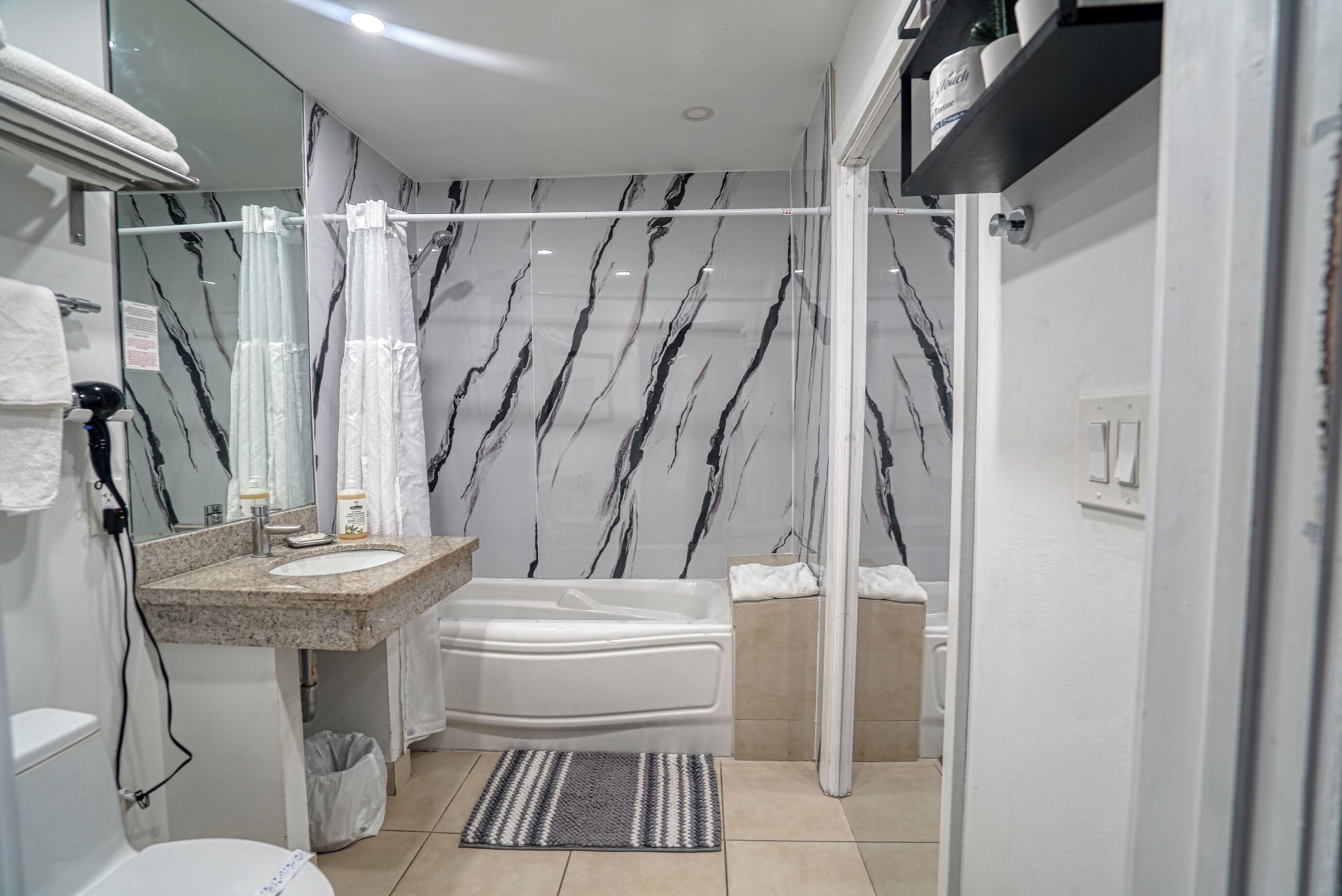 A modern bathroom with a marble-patterned wall, a built-in sink, a bathtub, and a shower area.