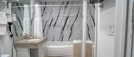 A modern bathroom with a marble-patterned wall, a built-in sink, a bathtub, and a shower area.