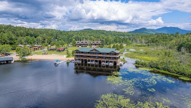 A lakeside lodge with multiple buildings, docked boats, and a forested backdrop.