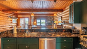 A log cabin kitchen with a granite countertop, stainless steel appliances, and green cabinets.