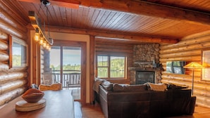 A log cabin interior with a stone fireplace, a leather sofa, and a dining table with a bowl.
