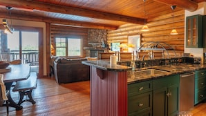 A wooden cabin interior with a kitchen, dining area, and a stone fireplace.