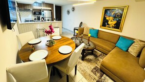 Una sala moderna con un sofá marrón, una mesa de comedor preparada para cuatro comensales y una cocina al fondo.