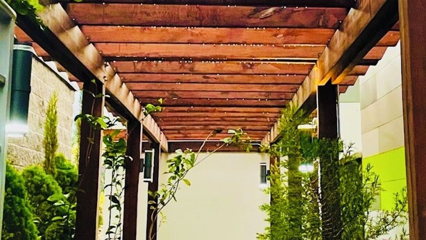 Un paseo techado con suelo de baldosas, bordeado por follaje y una pared de piedra.