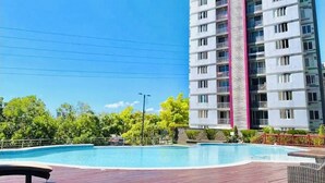 Una piscina con cubierta de madera, rodeada de follaje y un edificio residencial alto con balcones.