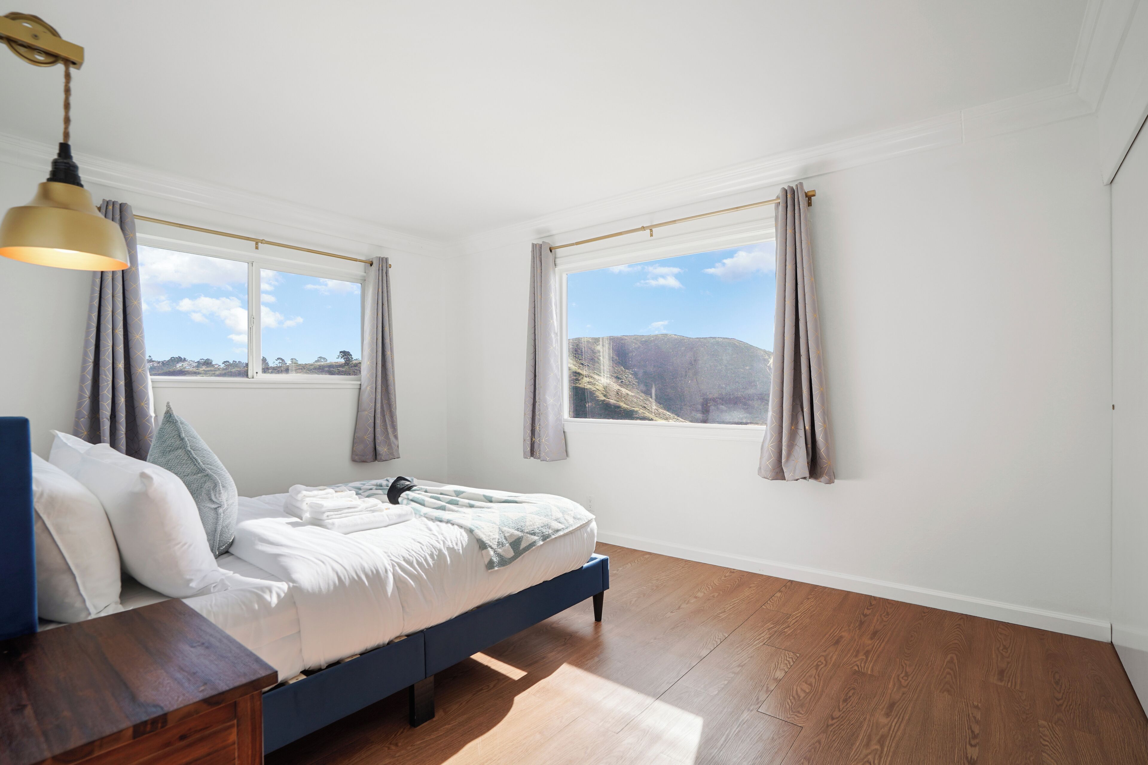 Un dormitorio con cama, suelo de madera y ventanas grandes con cortinas.