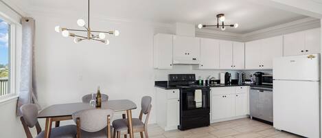 A modern kitchen with white cabinets, a black stove, and a dining area with a table and chairs.