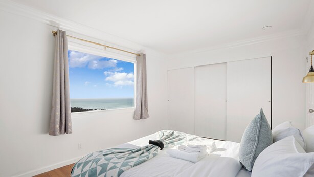 A bedroom with a bed, a window with curtains, a view of the sea, and a wardrobe. - Charming 2BR Coastal Getaway in Pacifica (Pacifica)