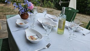 Mesa de comedor al aire libre con platos, vasos y una botella, rodeada de follaje y una vista panorámica.