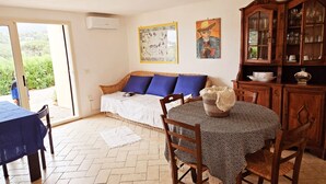 Un cuarto acogedor con un sofá de mimbre, una mesa de comedor con sillas, un armario con puertas de cristal y una ventana con vistas a la vegetación.