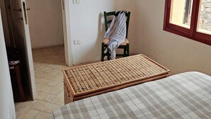 Un dormitorio con una cama, una silla, una ventana y un cuadro en la pared.