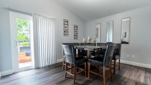 A dining room with a large table and six chairs, a sliding glass door leading to an outdoor area, and decorative wall art.