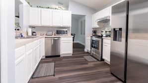 A modern kitchen with white cabinetry, stainless steel appliances, and a wooden floor.