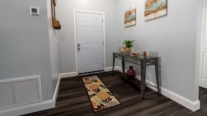 A hallway with a white door, a glass console table with decorative items, and two landscape paintings on the wall.