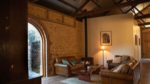 Un salon chaleureux avec des murs en pierre, des canapés en cuir, une cheminée et une grande fenêtre.