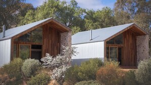 Une maison moderne à deux étages, dotée de grandes fenêtres et d’un toit en pente, entourée d’une végétation luxuriante.