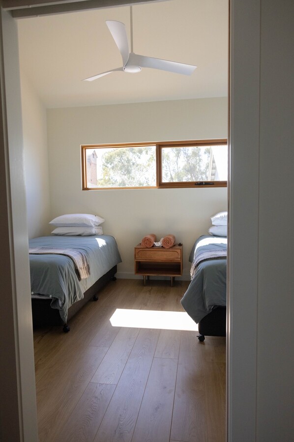 Un dormitorio con dos camas, ventilador de techo, ventana y suelo de madera.