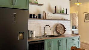 Une cuisine équipée d’un réfrigérateur encastré, d’un four à micro-ondes et d’un évier. Il y a une horloge au mur et des étagères avec des bouteilles et des verres.