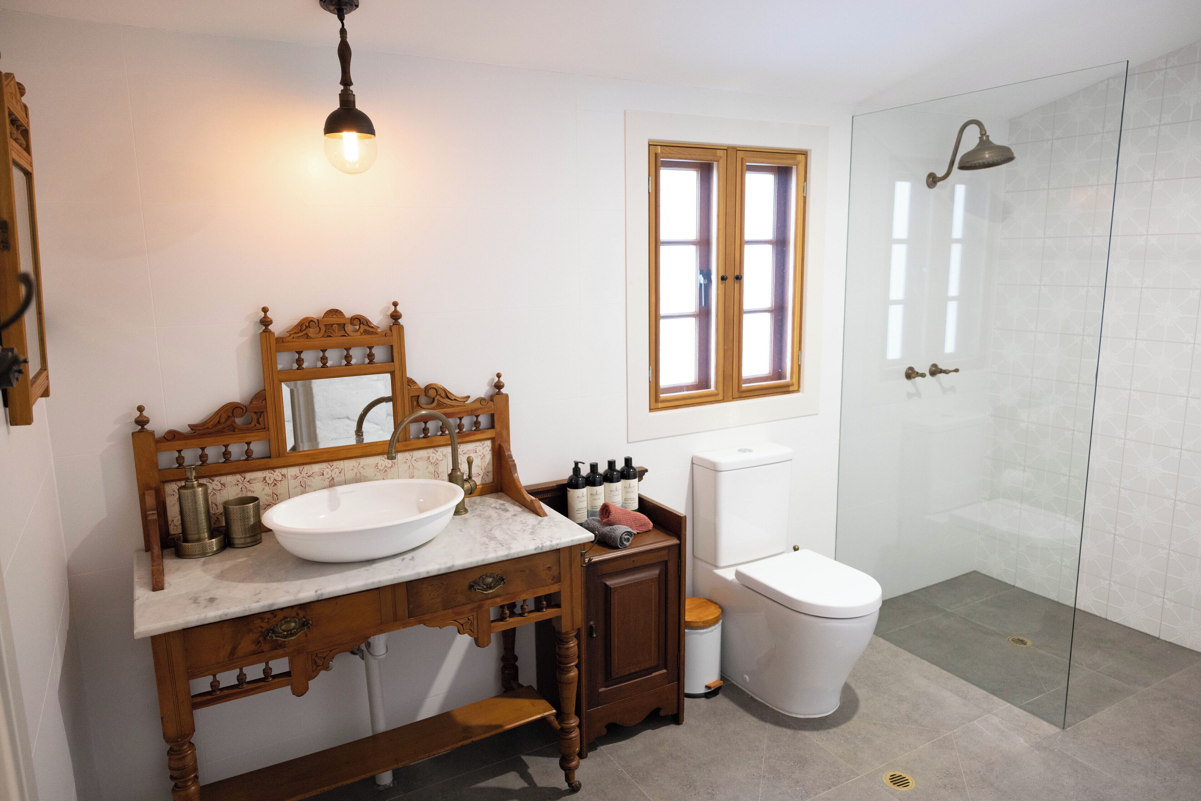 A bathroom with a wooden vanity, a large mirror, a white sink, a toilet, and a glass-enclosed shower area.