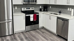 A modern kitchen with white cabinets, stainless steel appliances, and a grey tiled backsplash.