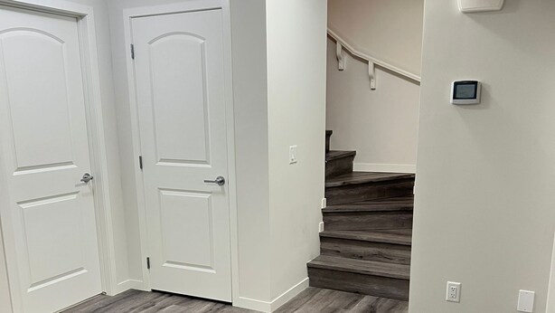 A hallway with wooden flooring, white walls, and a staircase leading to another floor.