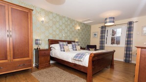 A bedroom with a wooden bed, a wardrobe, a nightstand, a lamp, and a window with curtains.
