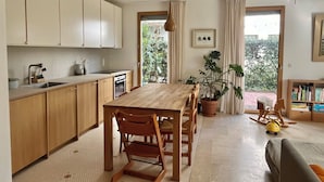 Cocina moderna con armarios de madera, una mesa de comedor con sillas, una planta en maceta y vistas al exterior.