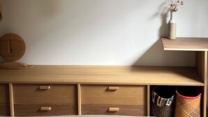 Una habitación con un aparador de madera, un perchero y un florero con flores secas sobre una estantería.