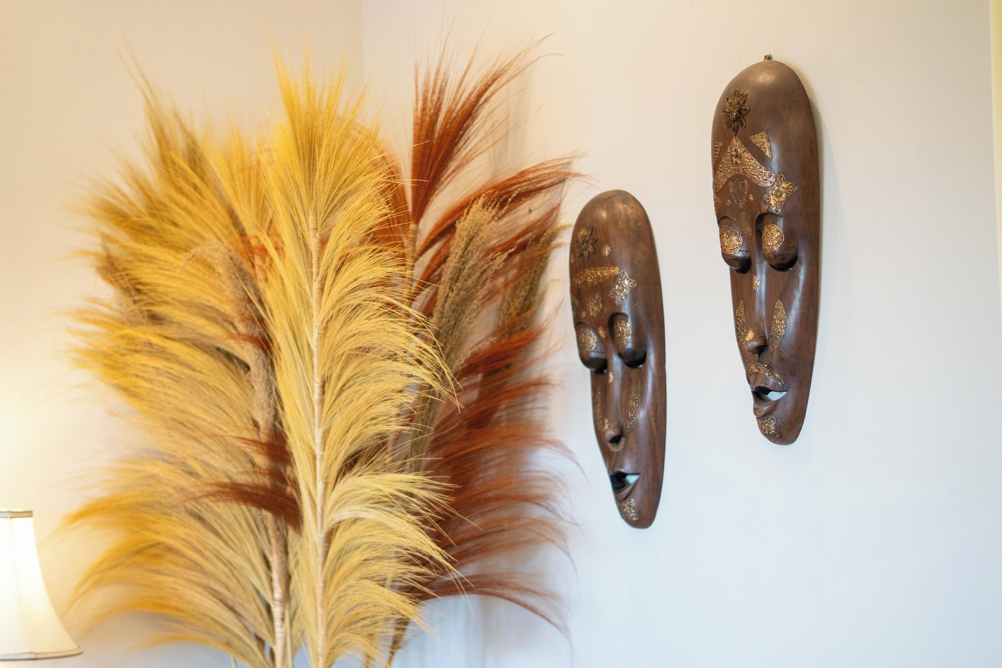 A wall with two wooden masks and a large feather arrangement.