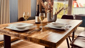 A wooden dining table set with white plates, cutlery, and a bottle of wine.