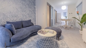 Una sala de estar moderna con un sofá gris, una mesa redonda de centro y un comedor con una mesa y sillas blancas.