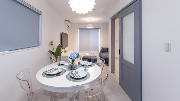 Un comedor moderno con una mesa redonda dispuesta para cuatro personas, sillas transparentes y una lámpara decorativa colgante.