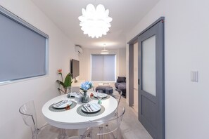 A modern dining area with a round table set for four, clear chairs, and a decorative light fixture above. - Nishikujo Maison Le Bleu Chigusa (Osaka)