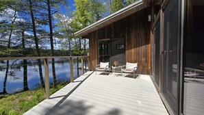 Une terrasse en bois avec deux chaises et une table, donnant sur un lac paisible bordé d’arbres.