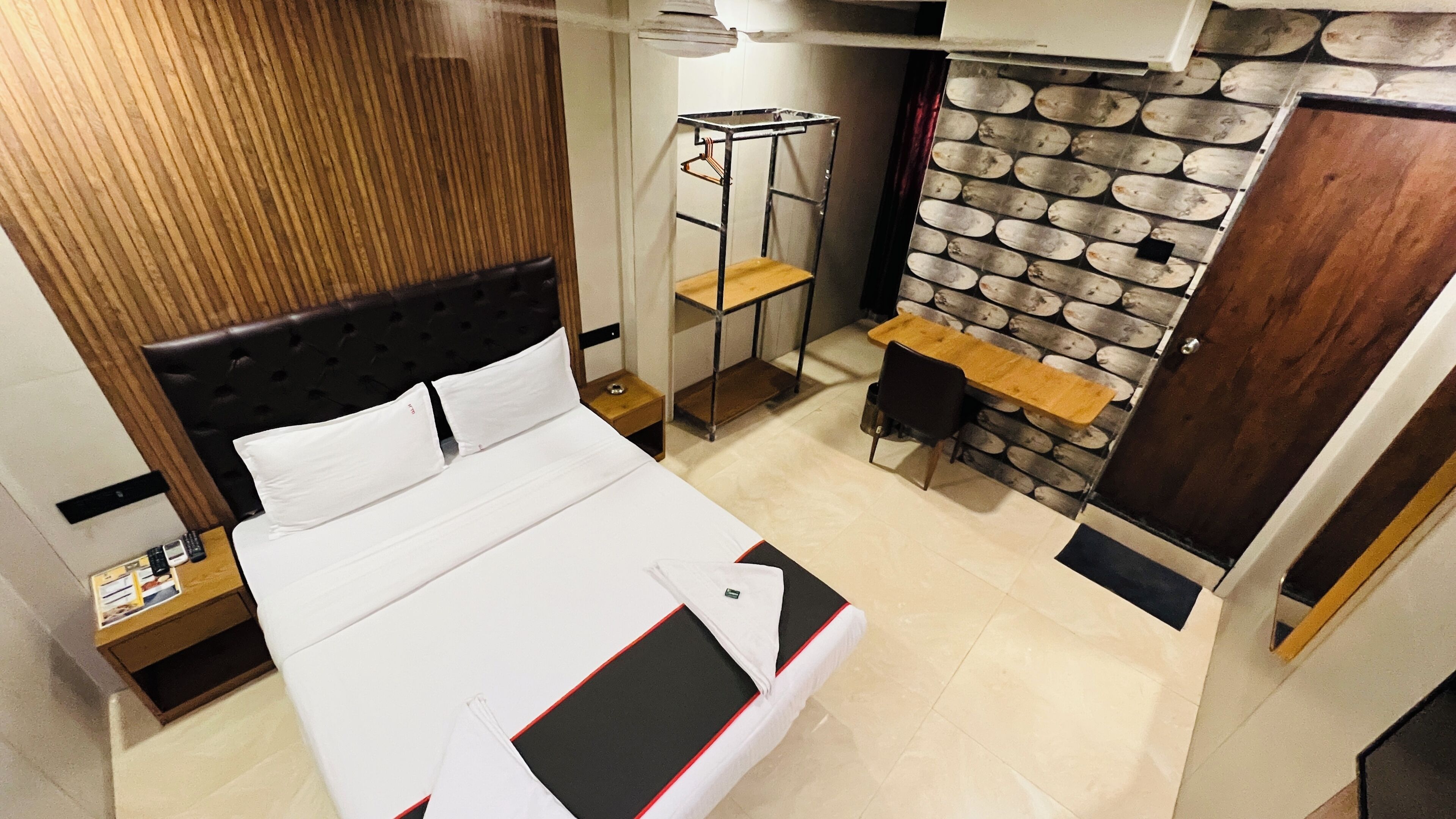 A hotel room with a bed, a small table, a chair, a wardrobe, and a wall with a patterned design.