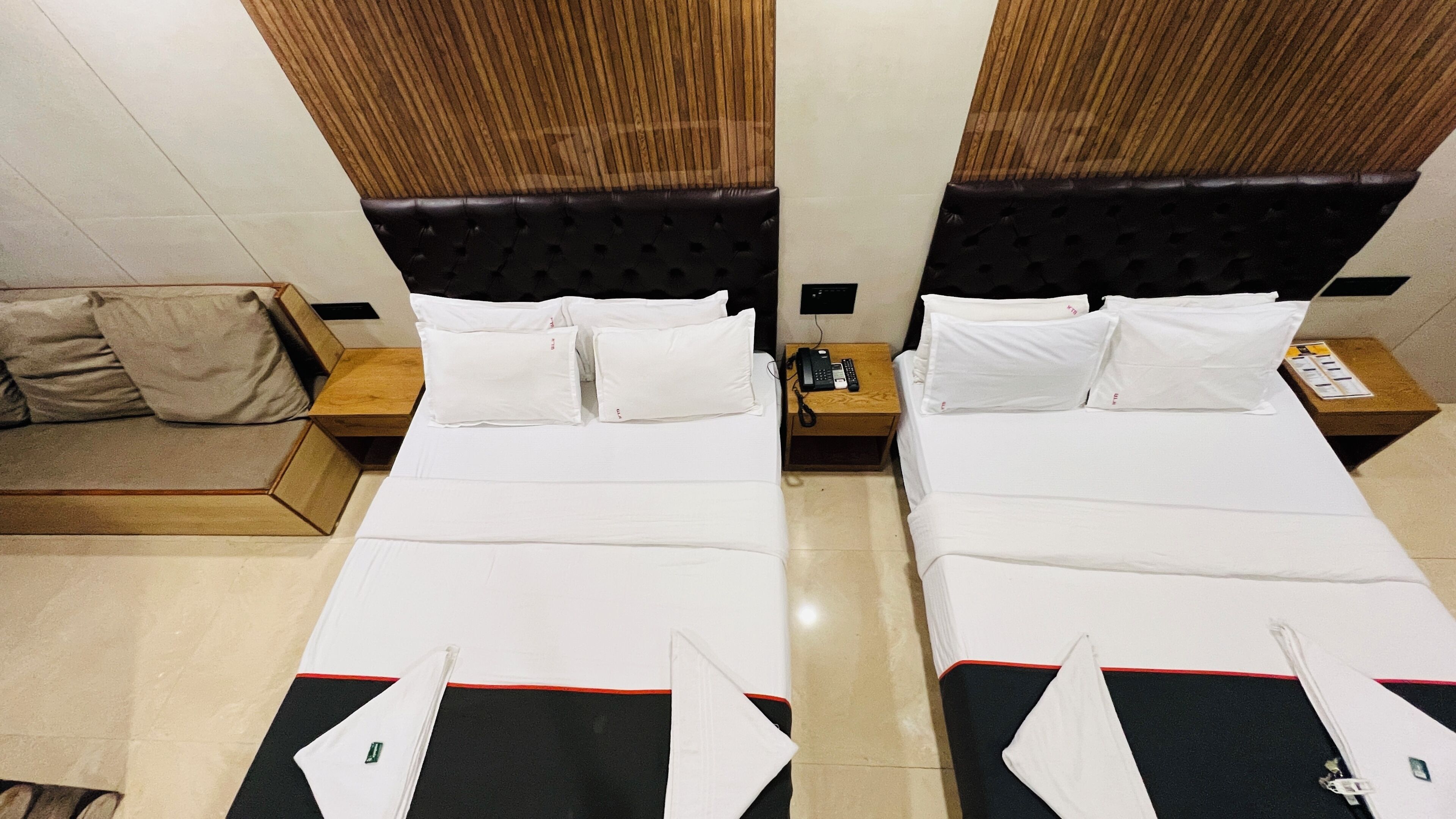 Habitació d'hotel amb dos llits, un panell de capçalera de fusta, una meseta de nit amb un telèfon i una taula de fusta petita.