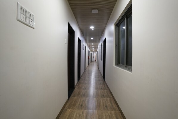 A long, narrow hallway with a wooden floor, white walls, and black doors. - U LIFE HOTEL (Mumbai)