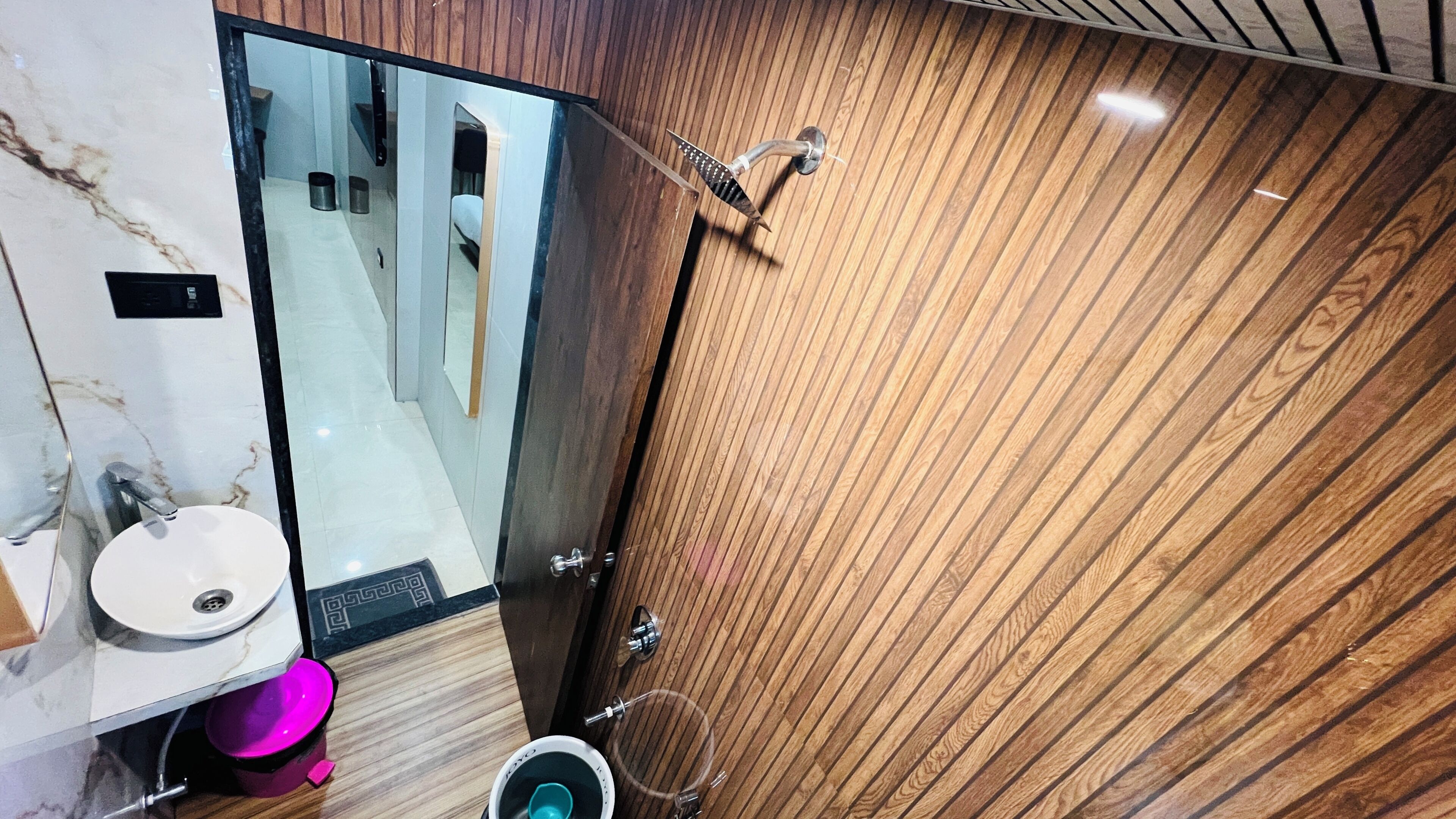 Une salle de bain moderne avec un lavabo en marbre, un meuble-lavabo en bois, un miroir et une douche dotée d’une porte en bois.