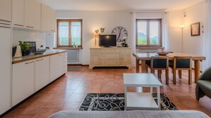 Een moderne keuken met witte kastjes, een eethoek met tafel en stoelen, een televisie en een klok aan de muur.