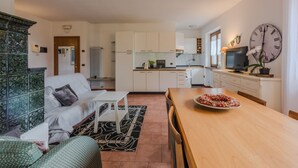 Een modern appartement met een woonkamer, keuken en eethoek. Het heeft een grote klok, een televisie en een sierplant.