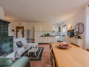 Eine moderne Wohnung mit Wohnzimmer, Küche und Essbereich. Sie verfügt über eine große Uhr, einen Fernseher und eine Zierpflanze.